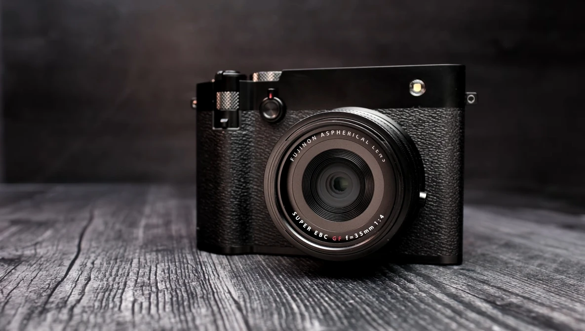 Black rangefinder camera with textured leather body on weathered wooden surface.