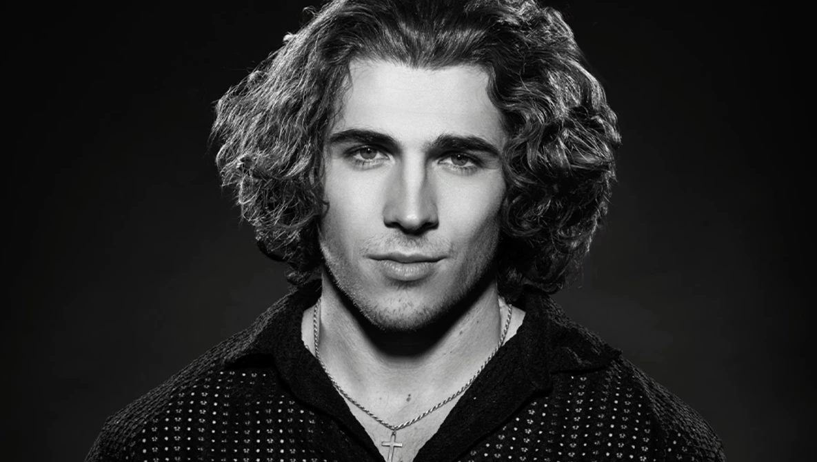 Black and white portrait of a man with shoulder-length curly hair and a chain necklace.