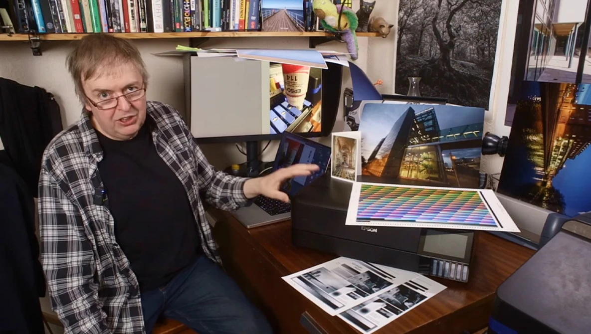 Photographer reviewing color-graded prints and digital displays at a desk workspace.