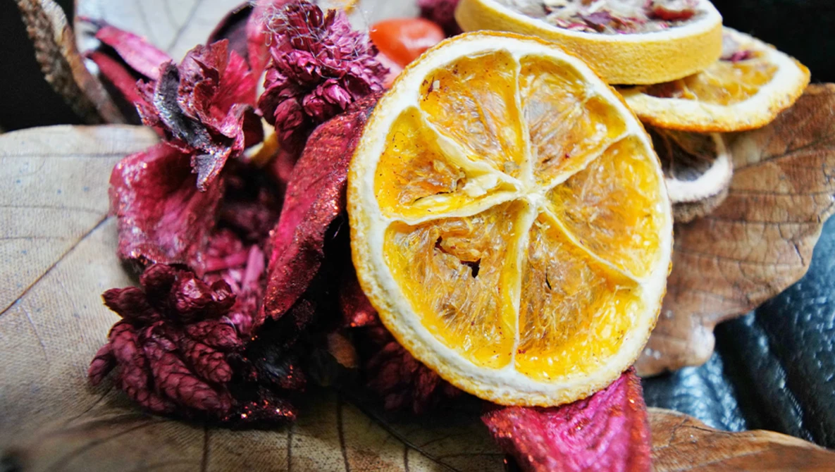 Dried citrus slices and dried flower petals arranged on a wooden surface.