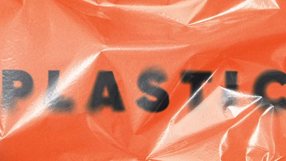 Plastic-wrapped orange surface with partial black text reading "PLAST" visible through the wrinkles and folds.