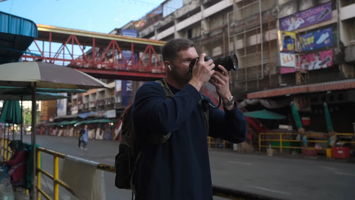 Photographer holding camera to face while standing in urban amusement park setting.