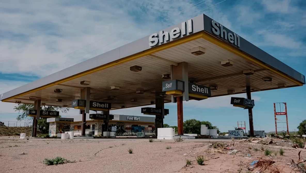 Abandoned Shell gas station with weathered canopy under blue sky amid desert terrain.