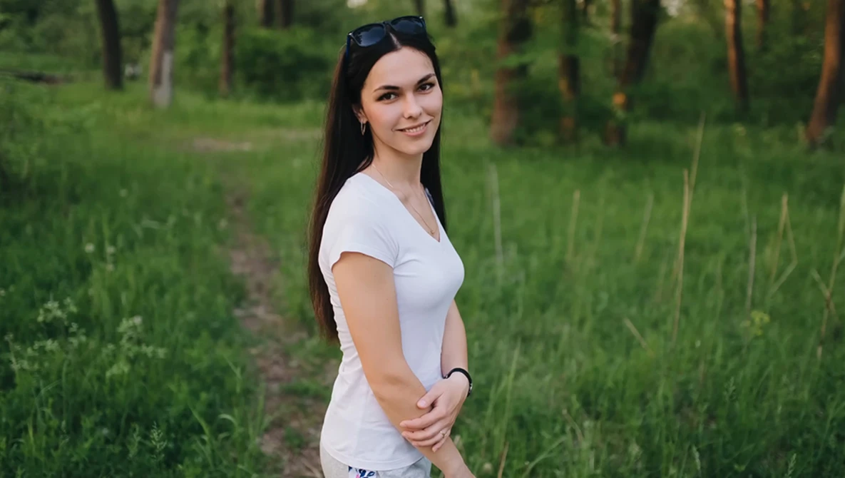 Woman in white t-shirt standing on a forest path with sunglasses on her head.