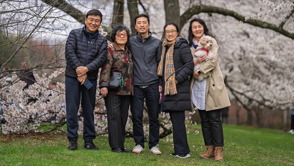 Five people standing together on grass beneath blooming cherry blossom trees.