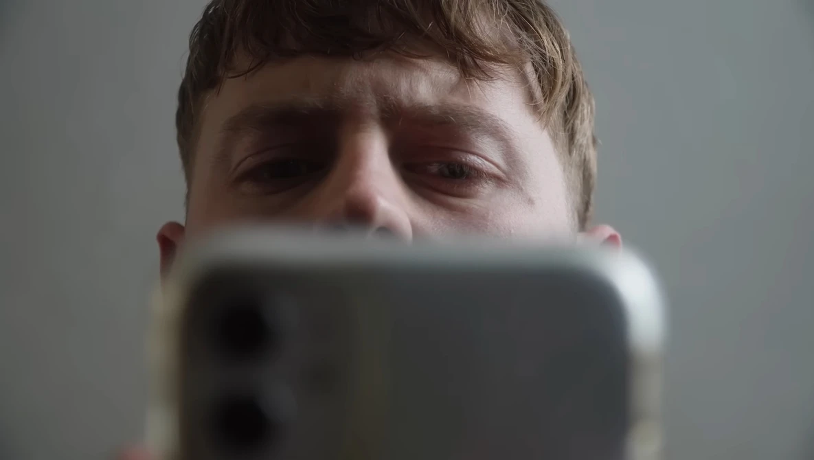 Person holding smartphone up to face, partially obscuring features while looking down at screen.