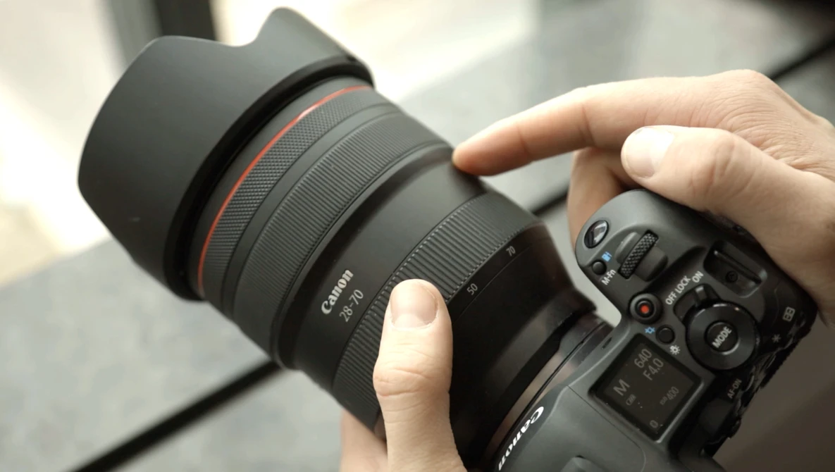 Photographer's hands holding a Canon RF-mount telephoto lens attached to a mirrorless camera body.