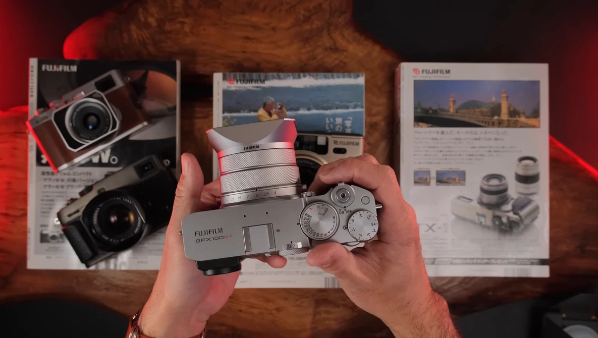 Hands holding a vintage compact rangefinder camera with product brochures and additional camera equipment displayed on a wooden surface.