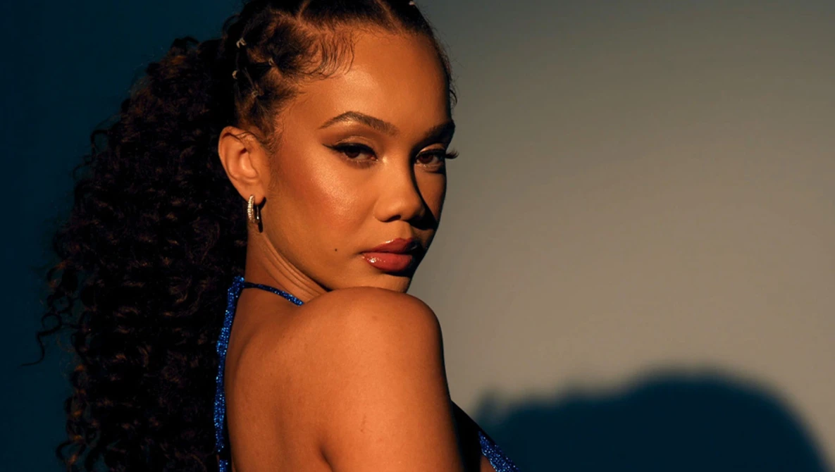 Woman with long curly hair looking over shoulder against blue and warm lighting backdrop.