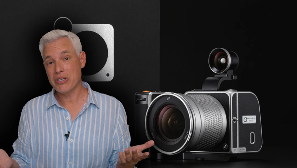 Man in striped shirt discussing camera equipment displayed against black background.