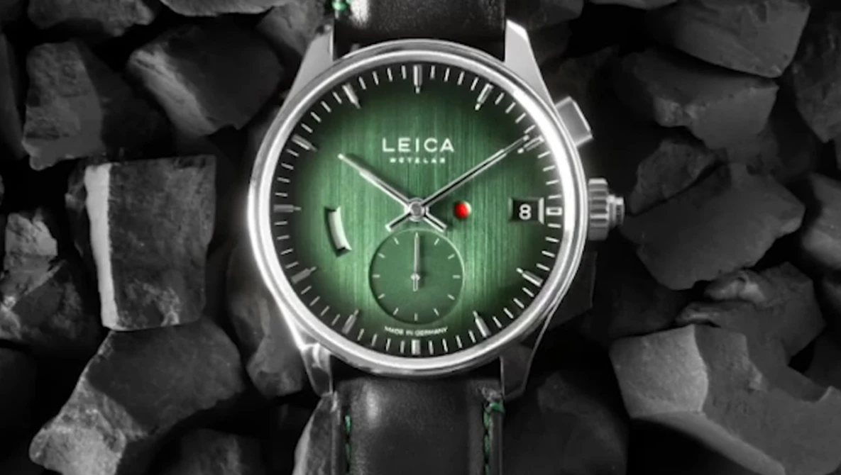 Leica chronograph watch with green dial and black leather strap on textured stone background.