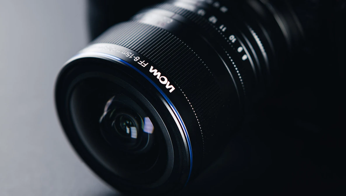 Wide-angle camera lens with blue accent ring mounted at an angle against a neutral gray background.