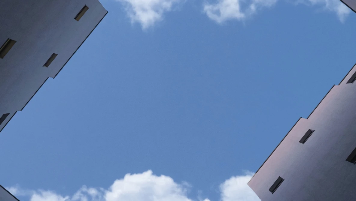 Looking upward between two white apartment buildings framing a blue sky with white clouds.