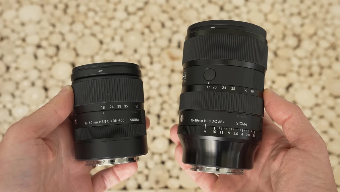 Two camera lenses held side-by-side for comparison, with the right lens noticeably larger than the left.