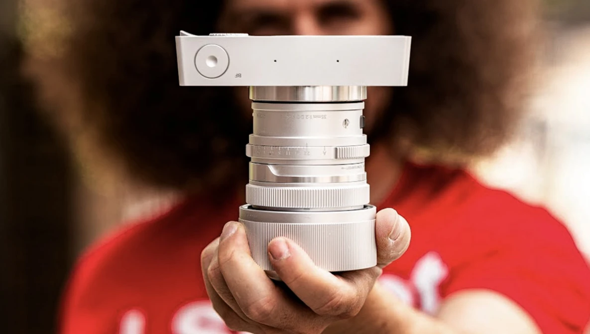 Hands holding a vintage rangefinder camera lens assembly with chrome barrel and focusing mechanism.