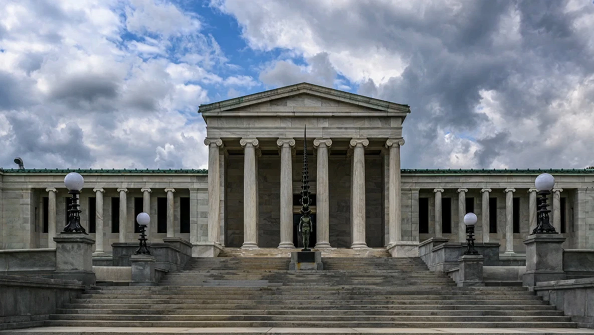 Neoclassical museum building with columned portico and symmetrical wings under partly cloudy sky.