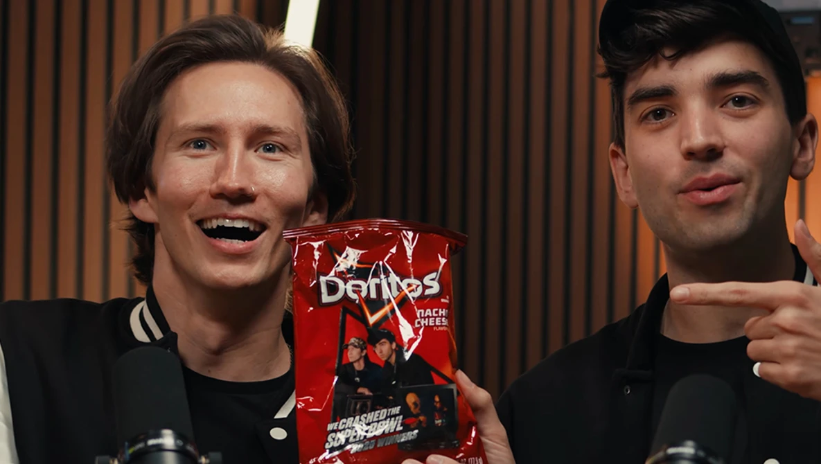 Two men in black clothing holding a red box product, smiling at camera in studio setting.