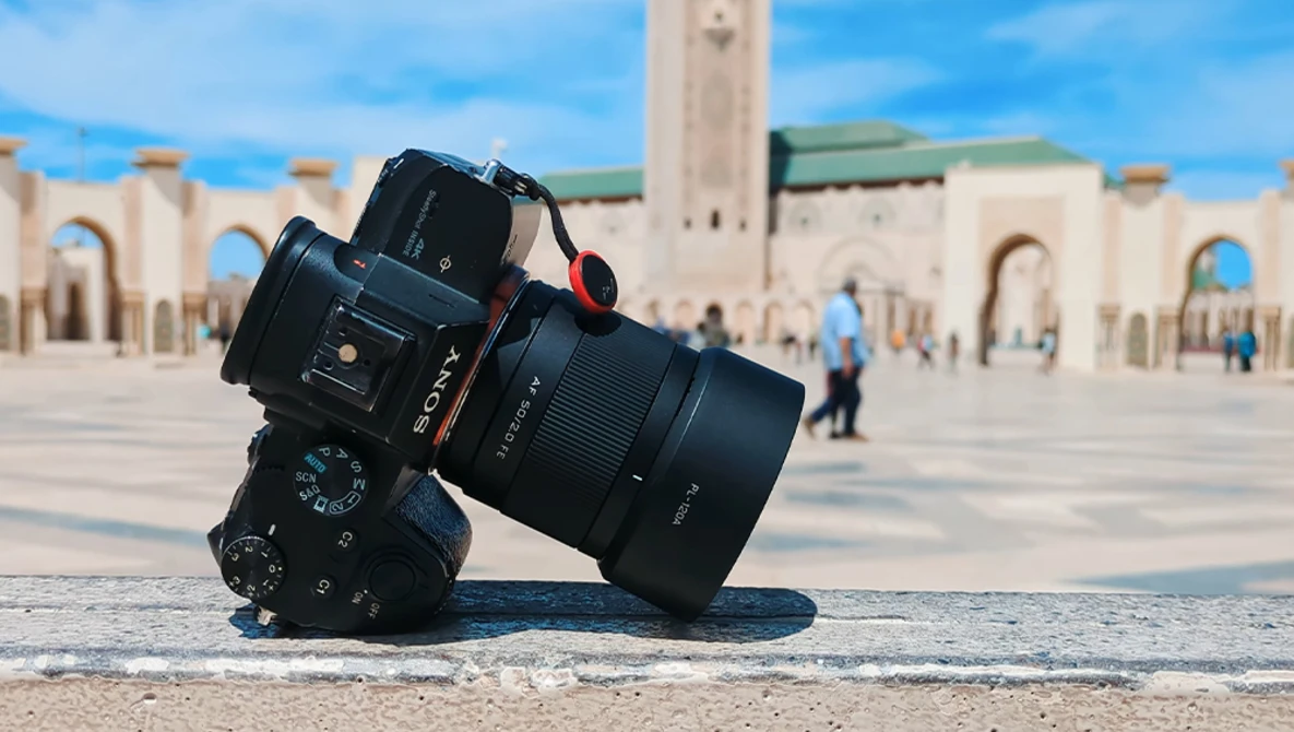 Camera with telephoto lens tilted on stone ground with mosque courtyard in background.