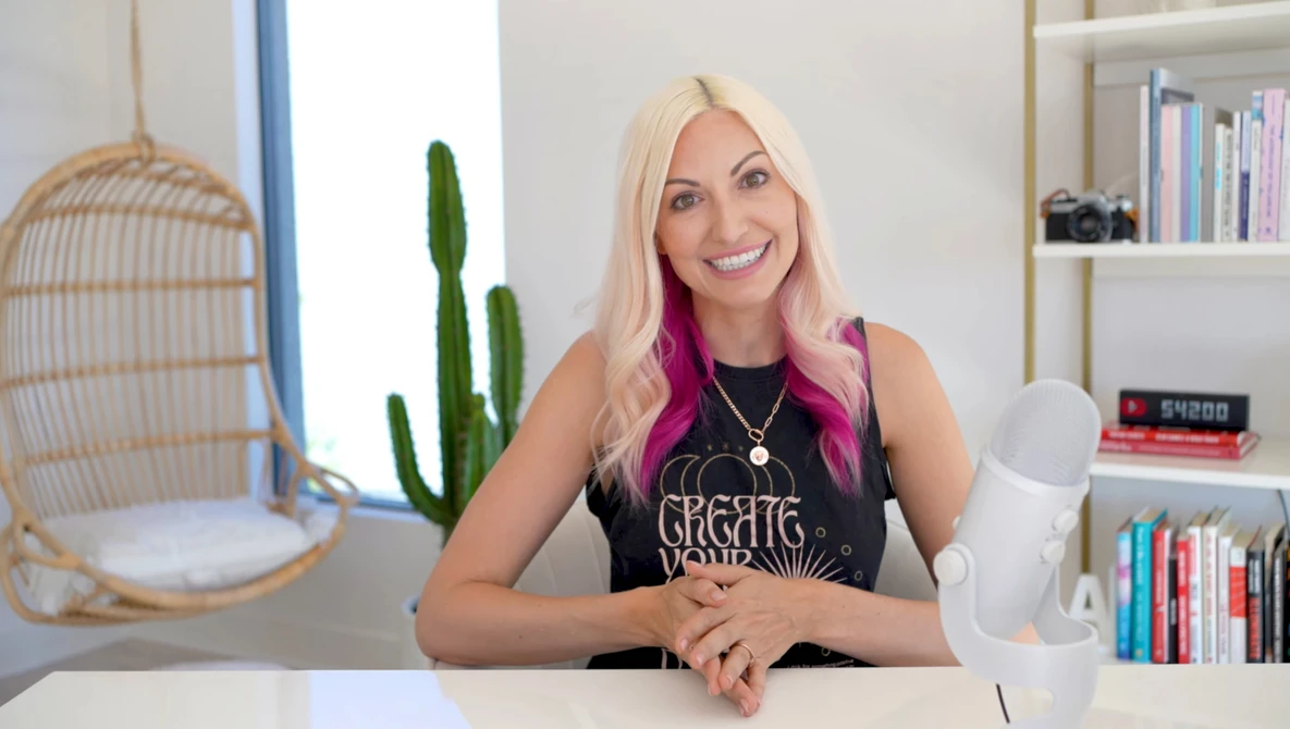 Woman with platinum blonde hair and pink underlights smiling at camera in bright studio setting.