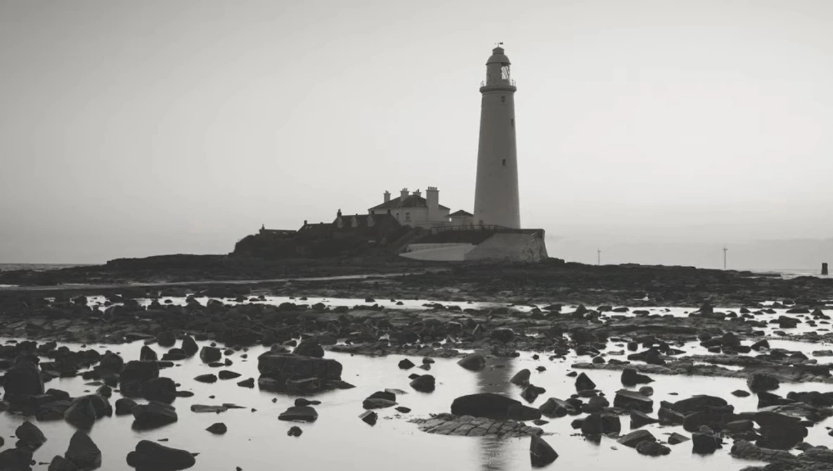 Lighthouse on rocky tidal flats under overcast sky in black and white.