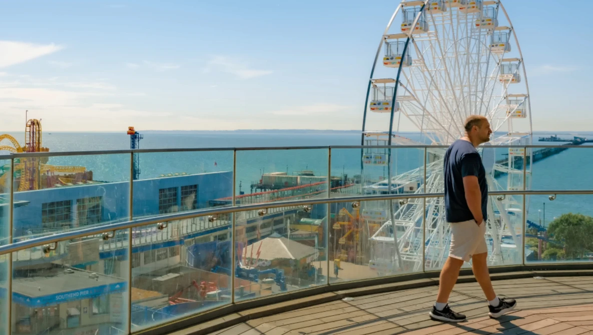 Runner jogging on a seaside boardwalk with a Ferris wheel and amusement park visible in the background.