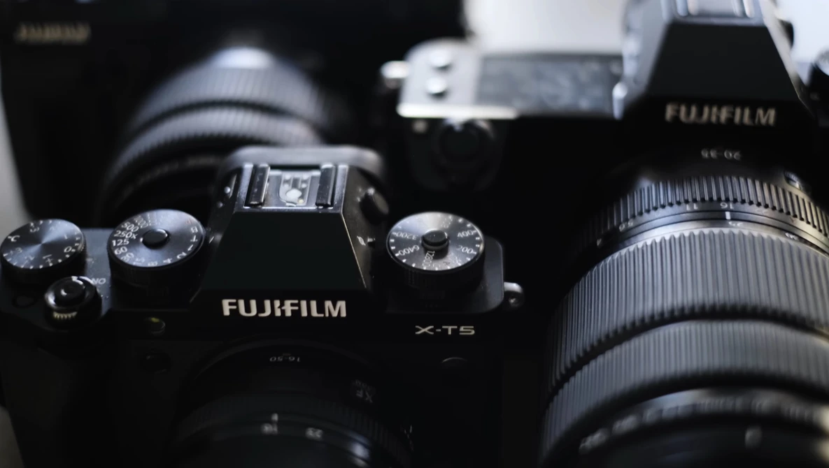 Fujifilm X-T5 camera with attached lens and additional camera gear in background.