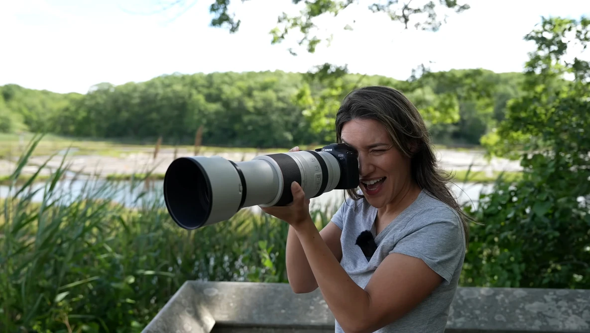 Photographer with telephoto lens overlooking a wetland landscape with reeds and trees.