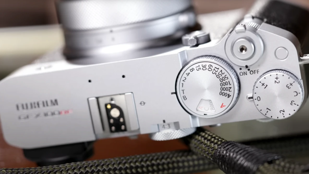 Top-down view of a white mirrorless camera with manual control dials and lens visible on textured fabric surface.