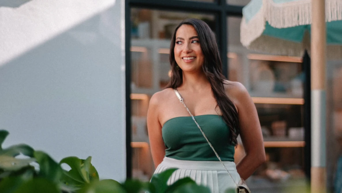 Woman in green halter top and white skirt smiling outdoors in natural sunlight.