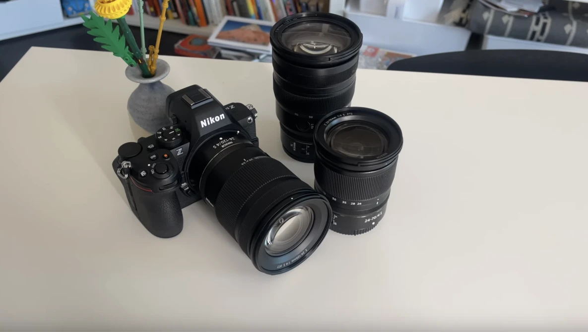 Nikon camera body with three interchangeable lenses arranged on a white surface.