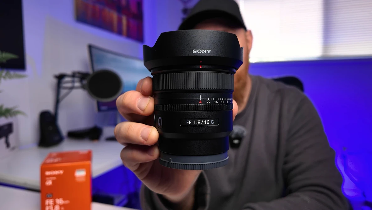 Sony lens with f/1.8/16 aperture being held up for display in a studio setting.