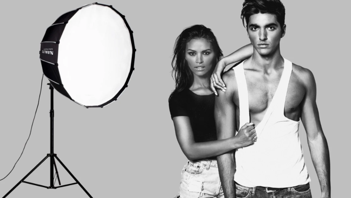 Two models pose together in a studio with a large softbox light positioned to the left.