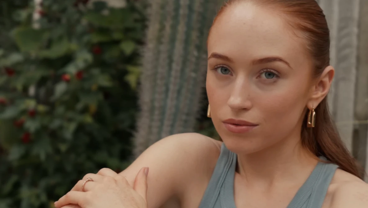 Woman with reddish-brown hair wearing a gray tank top, looking directly at camera with a neutral expression.