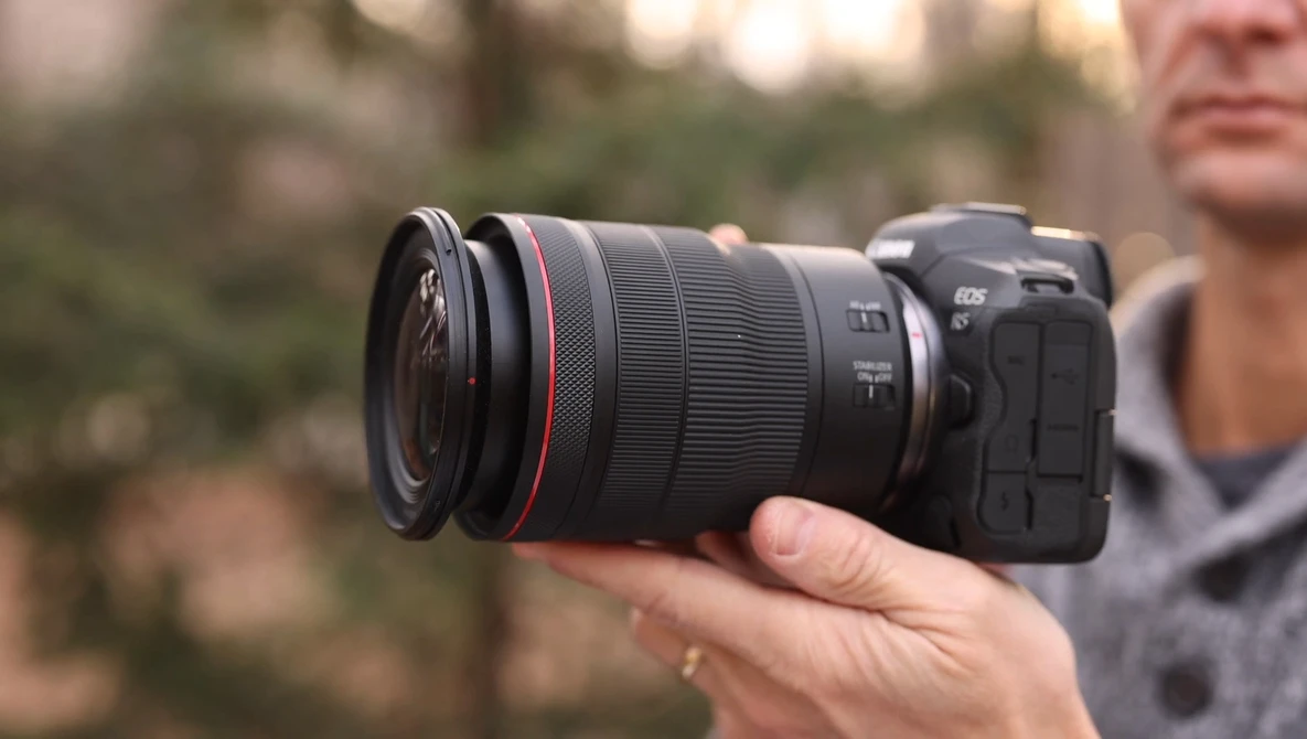 Photographer holding a Canon RF-mount mirrorless camera with a telephoto zoom lens attached.