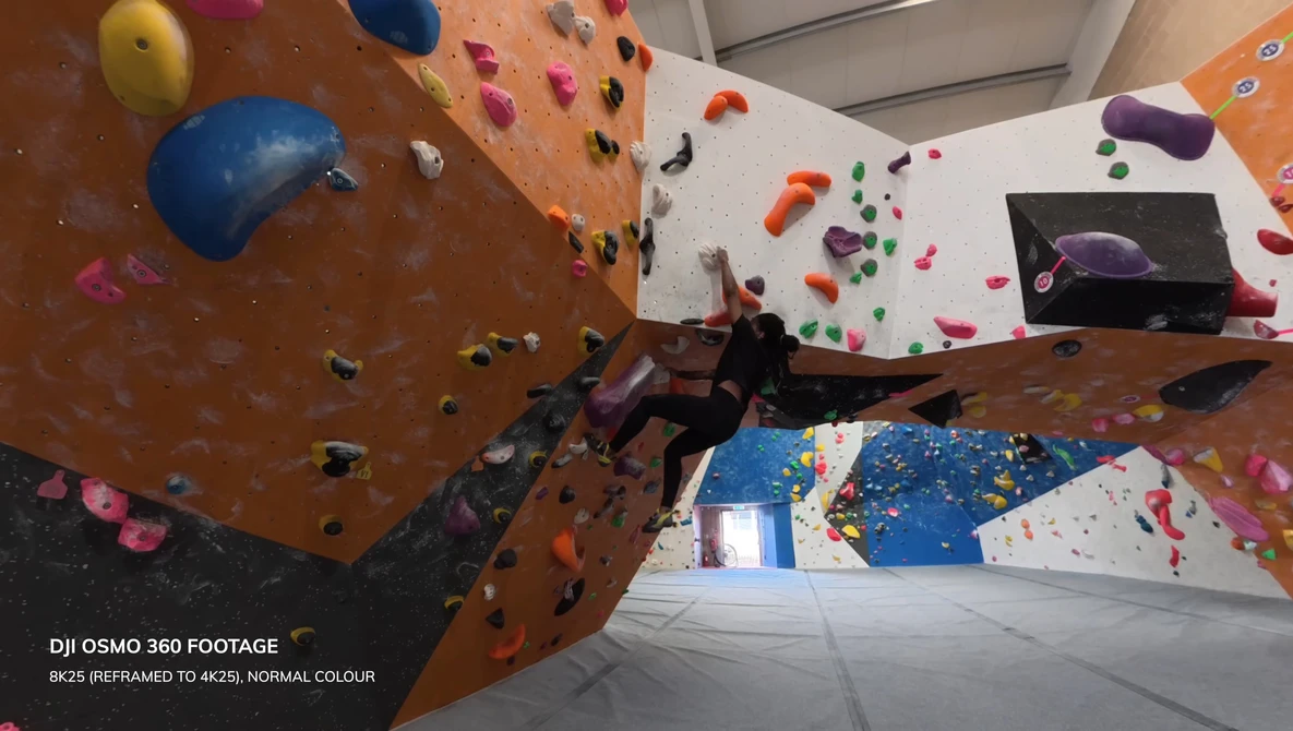 Indoor rock climbing wall with colorful holds viewed from below, showing multiple climbing routes and angles.