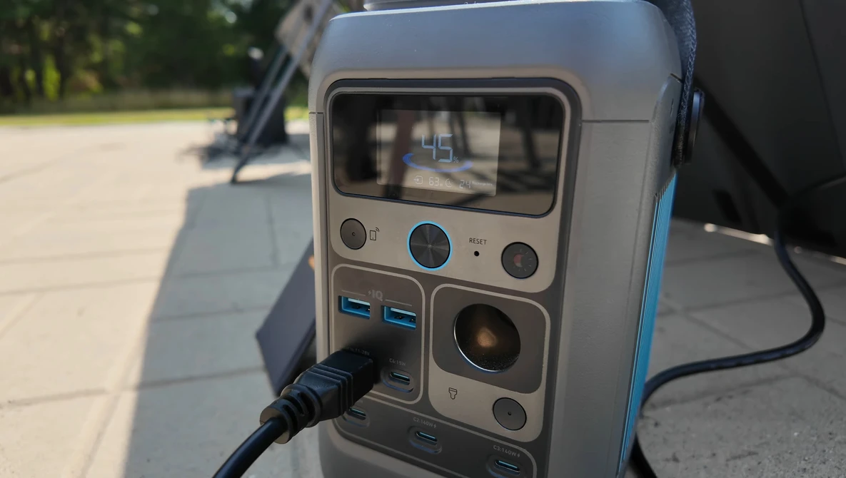 Portable power station with display screen, control buttons, and USB ports, photographed outdoors on pavement.