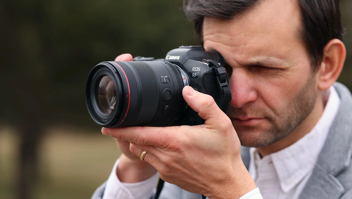 Photographer holding Canon EOS R5 mirrorless camera with RF lens to eye while composing shot.