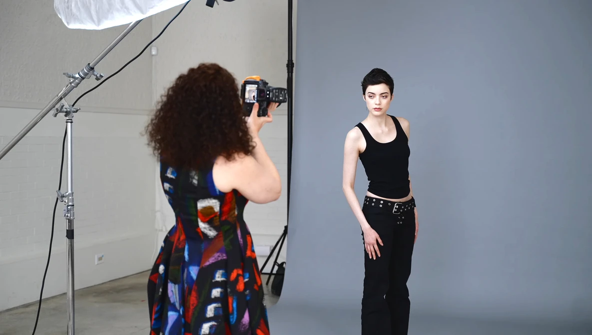 Photographer shooting a portrait of a woman in a studio with professional lighting setup.