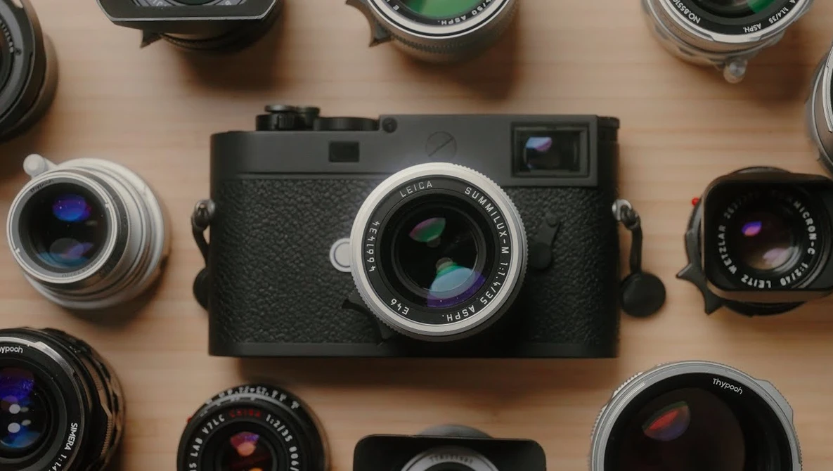 Rangefinder camera with interchangeable lenses arranged on wooden surface.