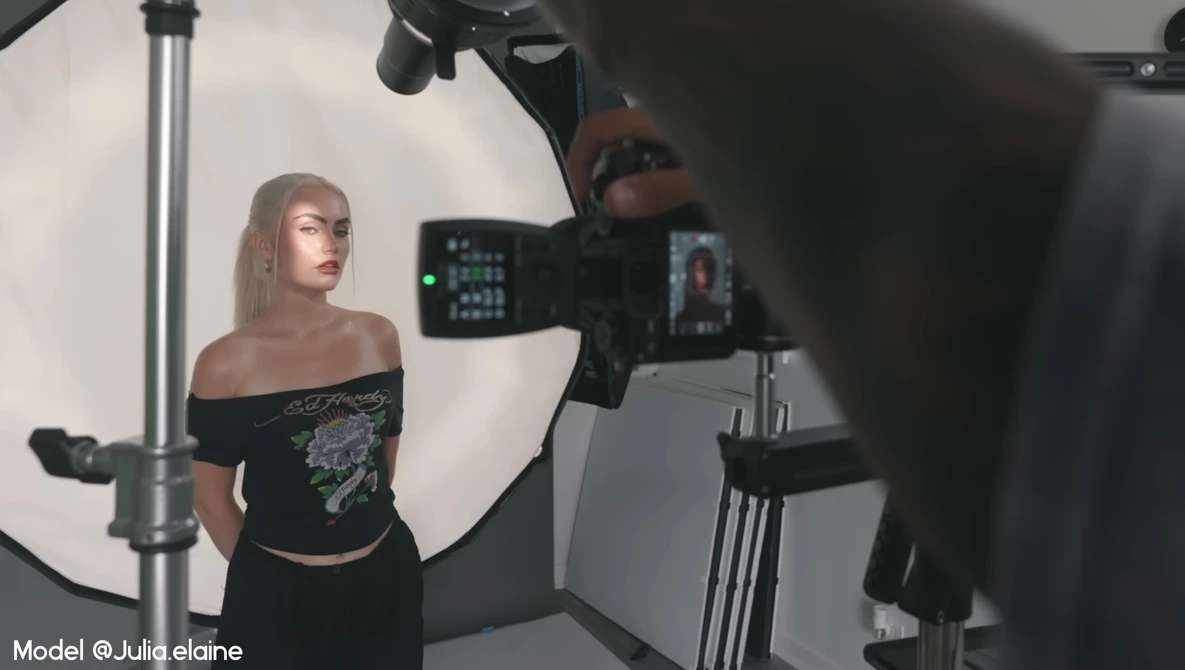 Model posing during studio photoshoot with professional cinema camera and large softbox lighting setup.