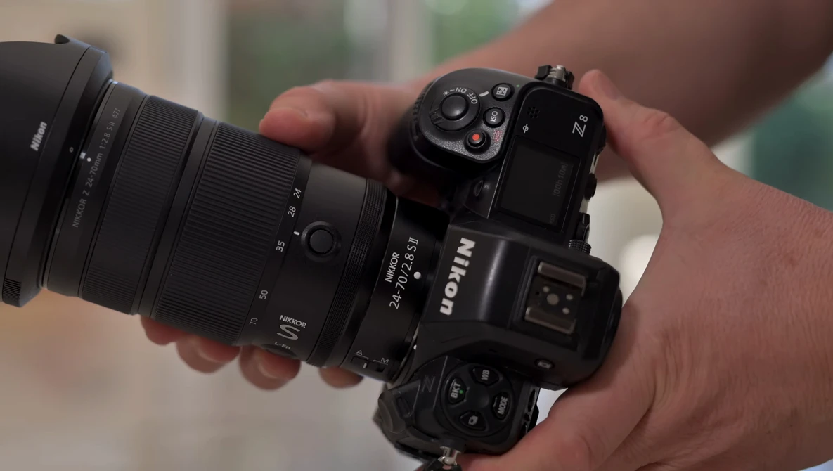 Hand holding a Nikon Z mirrorless camera with attached zoom lens in outdoor setting.