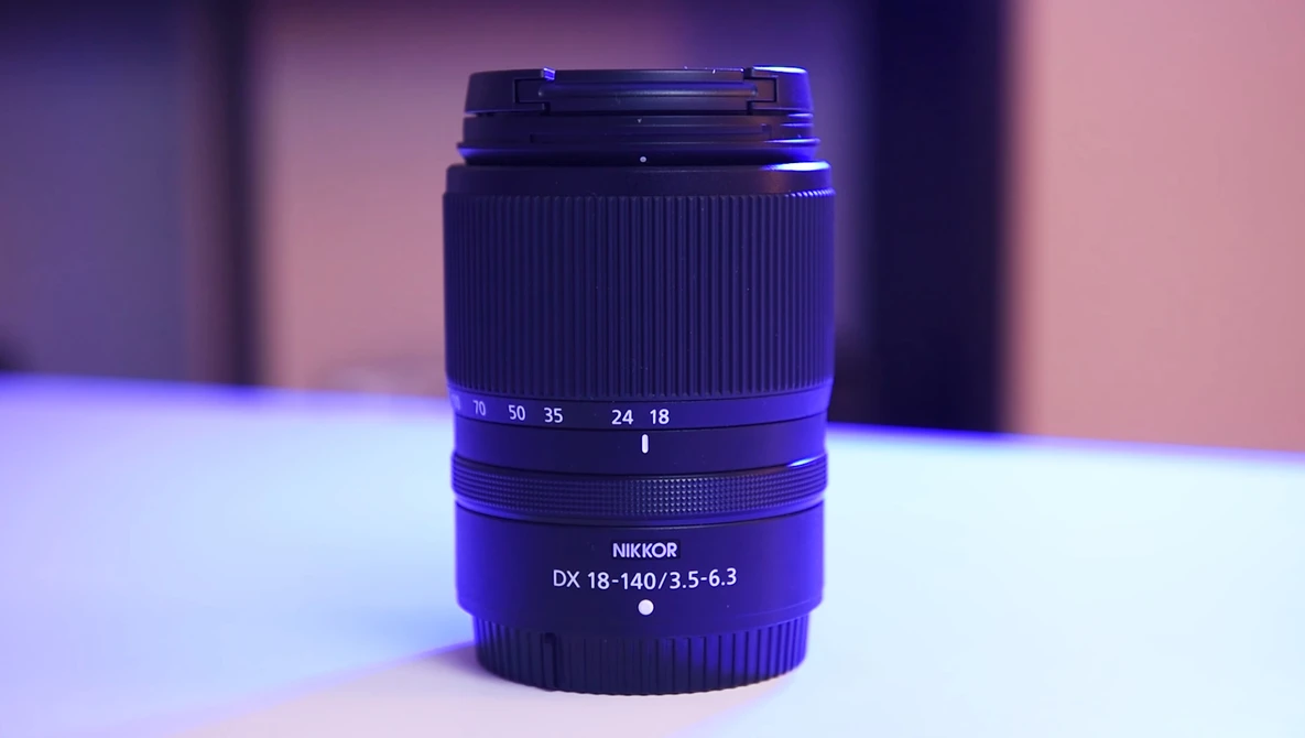 Nikon DX 18-140mm f/3.5-6.3 zoom lens with focus and zoom rings visible against purple and pink studio lighting.