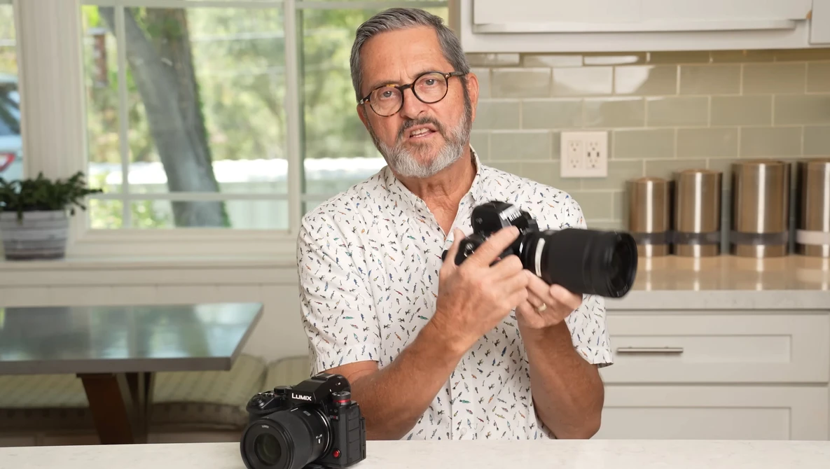 Photographer holding a camera with telephoto lens in a modern kitchen setting.