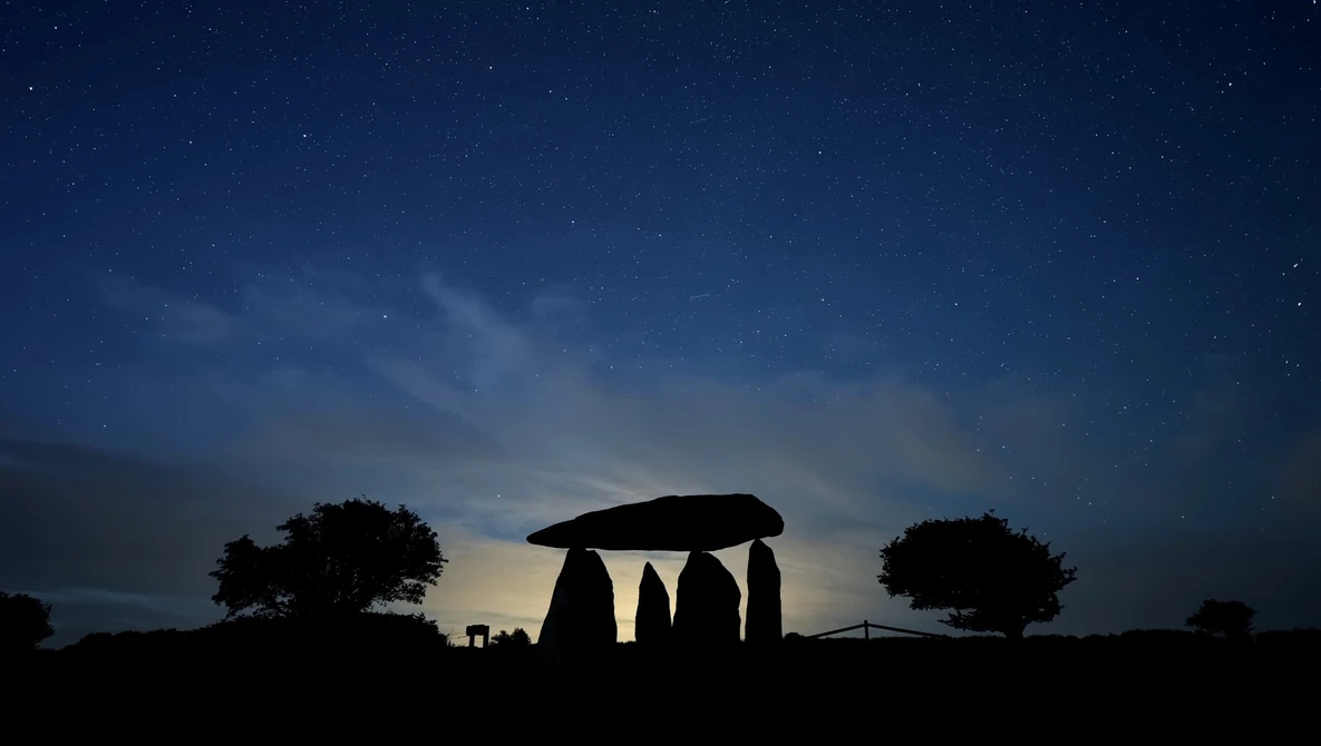 Silhouette of ancient stone monument against twilight sky with stars and surrounding trees.