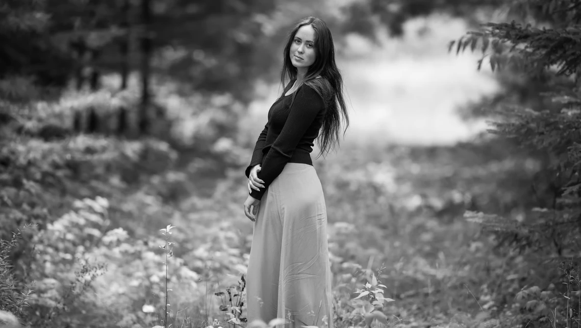 Woman in black top and light skirt standing in wildflower field, looking over shoulder.