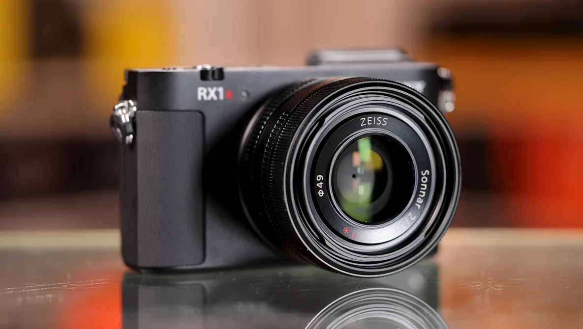 Sony RX1 compact camera with Zeiss lens on reflective surface against warm-toned background.