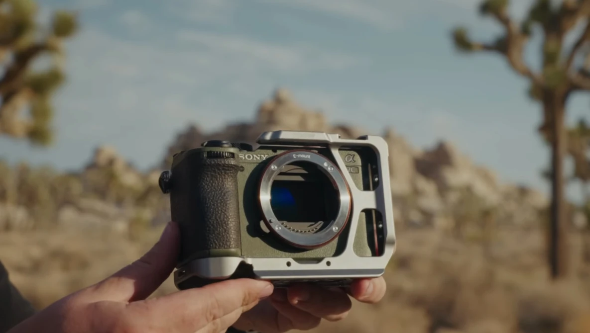Mirrorless camera body held in hand against desert landscape with Joshua trees.