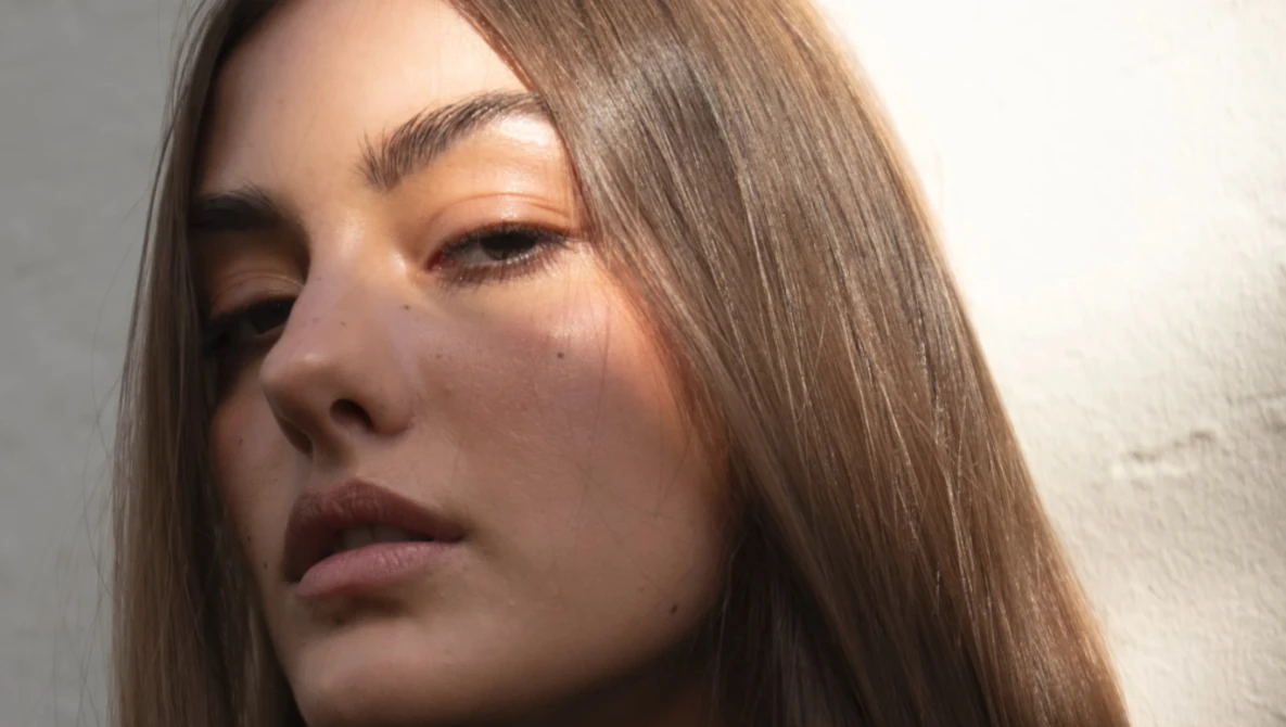 Woman with long brown hair gazing downward in soft, directional lighting.
