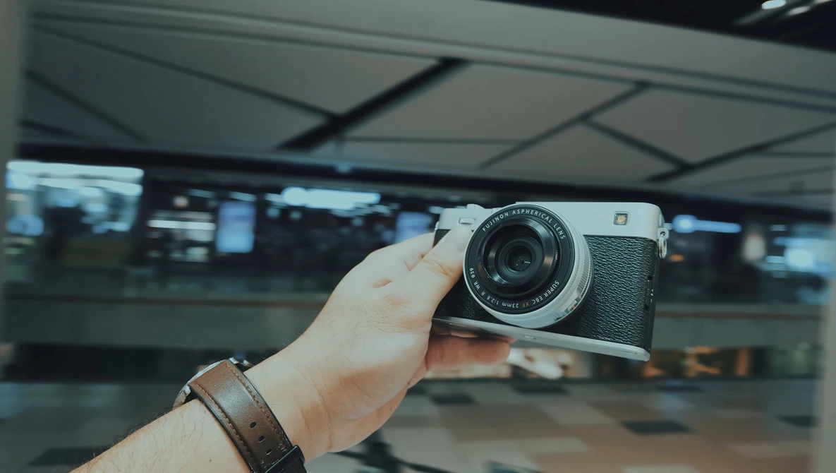 Person holding a vintage rangefinder camera with leather strap in an indoor terminal or station setting.