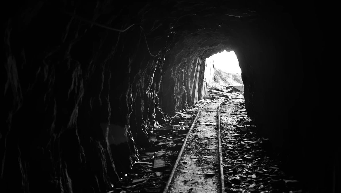 Railroad tracks disappearing into a dark tunnel with bright light visible at the far end.